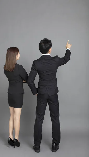 Vista trasera de hombre y mujer de negocios joven apuntando a la espalda gris —  Fotos de Stock