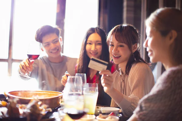 Felice giovane gruppo che mostra la carta di credito e chatta nel ristorante — Foto Stock