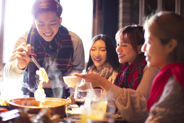 Felices jóvenes amigos comiendo olla caliente en el restaurante en invierno —  Fotos de Stock