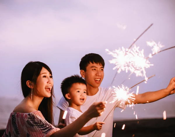 Família feliz celebrando o ano novo com faíscas na praia — Fotografia de Stock