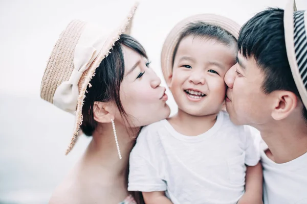 Счастливая семья целует ребенка на пляже — стоковое фото