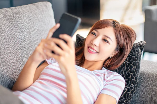 Mujer joven acostada en el sofá viendo el teléfono inteligente — Foto de Stock