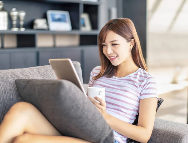 Sorrindo jovem mulher usando o tablet no sofá — Fotografia de Stock