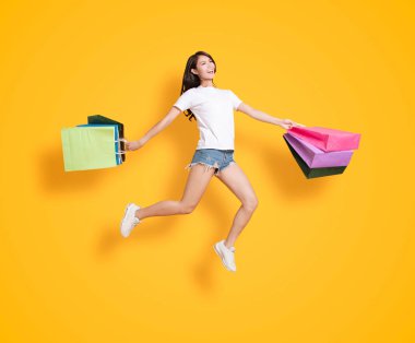 Alışveriş torbaları taşıyan ve zıplayan mutlu genç bir kadın. 