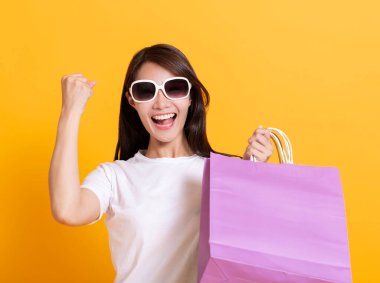Güneş gözlüklü genç bir kadın ve alışveriş torbalarını gösteriyor.