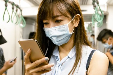 Metroda cerrahi maske takan genç Asyalı kadın.