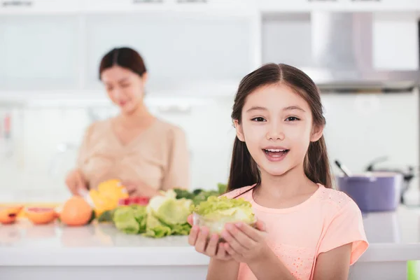 台所で働く母親と健康食品を見せる娘 — ストック写真