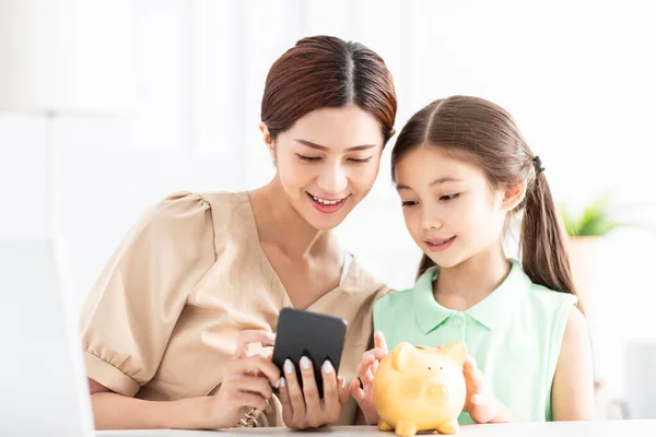 母親と娘と一緒に携帯電話を見て 彼女の将来の貯蓄のための貯金箱をチェック — ストック写真