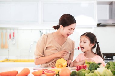 Mutlu anne ve kız sebze ve meyve yiyor.