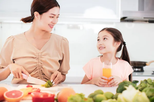 幸せな母と子供の娘キッチンで野菜や果物を準備 — ストック写真