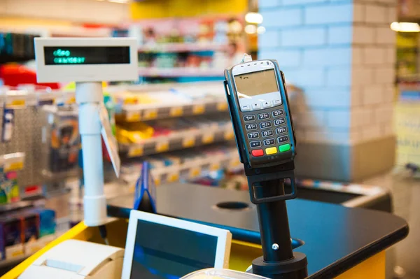 Empty cash desk with payment terminal and customers in queue in supermarket