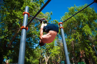 Delikanlı dışarıda yatay barda egzersiz yapıyor.