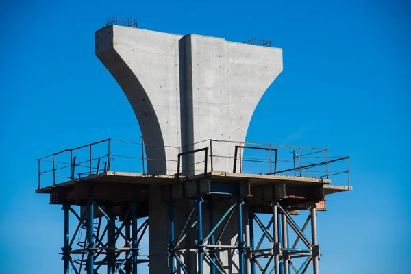 Construction of the interchange of a road bridge across the river. Builders and construction equipment on the construction site. The support of the bridge against the blue sky.