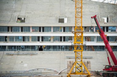 Stadyum inşaatı. Bir futbol stadyumunun inşaatı için inşaat malzemeleri ve işçiler. Koltuklar tribünde. Stadyumda çimensiz