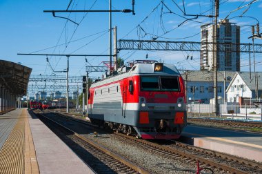 Tren raylarında ve demiryolu platformunda kırmızı tren lokomotifi. Tren ve tren istasyonu.