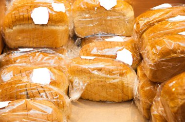 Bakkal rafında beyaz ekmek paketleri var.
