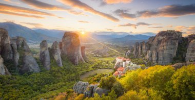 Yunanistan, Meteora 'nın gerçek güneş ve günbatımı gökyüzü ile romantik günbatımının panoramik manzarası. Meteora - inanılmaz kum taşı oluşumları. Meteora bölgesi UNESCO Dünya Mirası 'nda yer almaktadır.