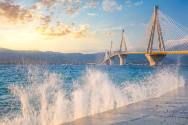 İnanılmaz manzara - Günbatımında modern köprü, dalgaların sıçramasıyla. Rion-Antirion Köprüsü, Yunanistan, Avrupa. Yunanistan 'daki Rion-Antirion Köprüsü dünyanın en uzun kablo destekli köprülerinden biri ve tamamen askıya alınmış türlerin en uzunu.