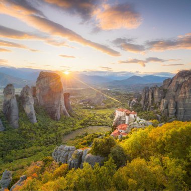 Landscape of Meteora, Greece at romantic sundown time with real sun and sunset sky. Meteora - incredible sandstone rock formations.  The Meteora area is on UNESCO World Heritage clipart