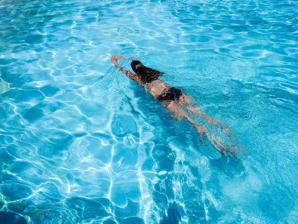 Güzel atletik güneş tatilde bir yüzme havuzunda yüzen kız tabaklanmış