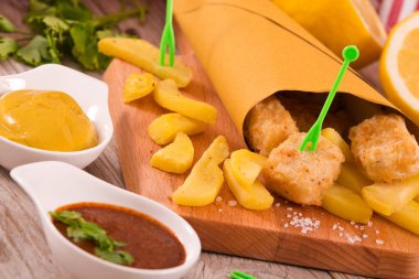 Balık ve cips kesme tahtası üzerinde hardallı.