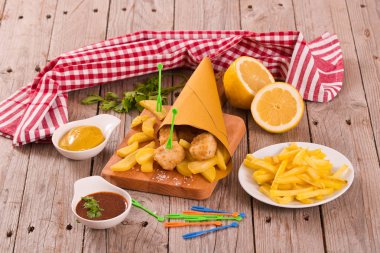 Balık ve cips kesme tahtası üzerinde hardallı.