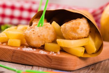 Balık ve cips kesme tahtası üzerinde hardallı.