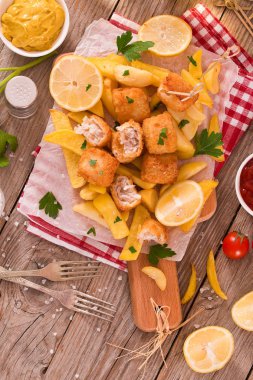 Kesme tahtasında patates kızartması ile balık ve cips.