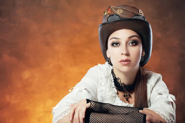 Beautiful woman in steampunk hat on painted orange colored background