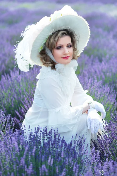 beautiful woman in victorian vintage style outfit and hat sitting on lavender field