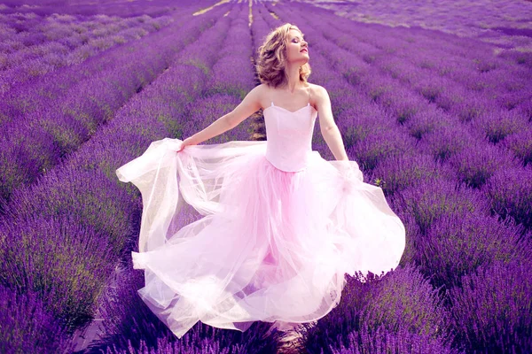美丽的女人在粉红色的礼服跳舞在薰衣草领域阳光明媚的夏天 — 图库照片