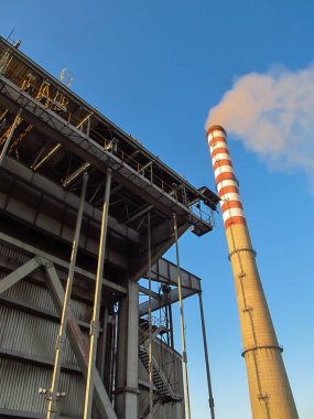 Uzun, beyaz ve kırmızı bir baca ve elektrik santralinin bir parçası.