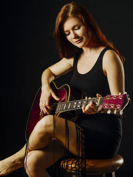 一个年轻漂亮的红发女人坐在弹吉他的照片 — 图库照片