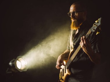Projektör önünde sahnede bas gitar çalmaya sakallı bir adam fotoğrafı.