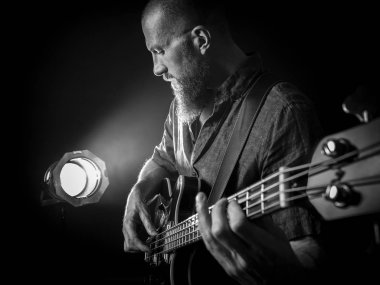 Projektör önünde sahnede bas gitar çalmaya sakallı bir adam fotoğrafı.