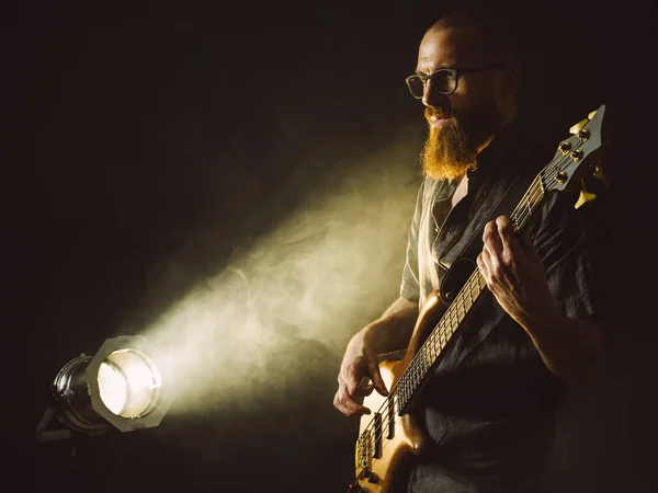 スポット ライトの前でステージ上でベースギターを演奏髭の男の写真 — ストック写真