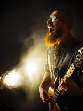 Çığlık atan bir bas gitarist Spot arka plan olarak karanlık bir kulüpte oynamaktan sakallı fotoğrafı.