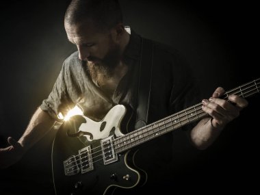 Sakallı bir adam bir spot ışığı önünde sahnede bas gitar çalmaya fotoğrafı.