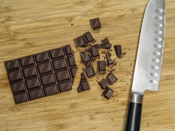 Bir Tablo Kısmen Kıyılmış Çikolata Pişirme Büyük Bir Bıçak Ile — Stok fotoğraf