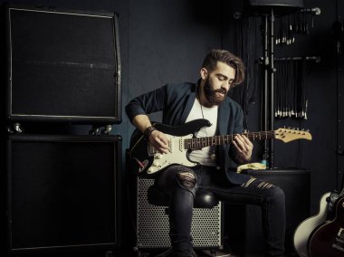 Bir kayıt stüdyosunda sakallı bir adamın oturup elektro gitarını çalarkenki fotoğrafı, gülümse.,,,