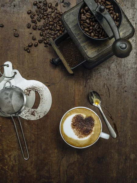 图为一张凌乱的乡村木桌咖啡豆 磨床和一杯带有心形巧克力的咖啡 — 图库照片