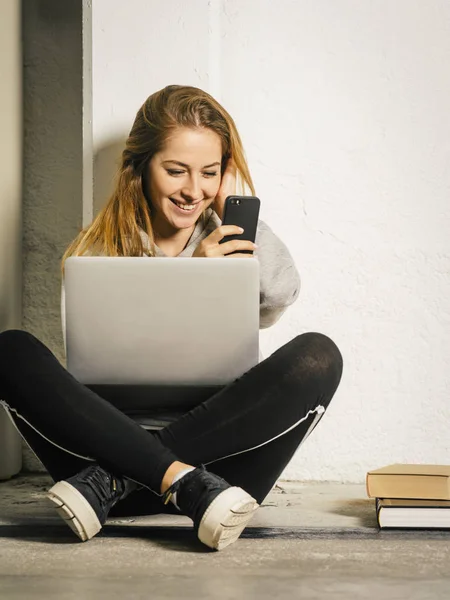 Photo Young Woman Sitting Hallway Laptop Laughing Message Her Smartphone — Stock Photo, Image