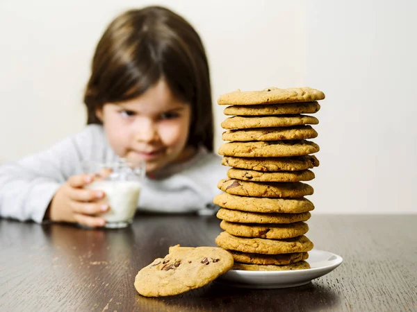 照片上 一个小女孩拿着一杯牛奶 凝视着一大堆巧克力饼干 专注于饼干 — 图库照片