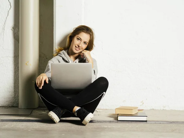 Mladý šťastný student pracuje na svém laptopu na školní chodbě — Stock fotografie