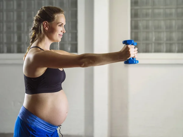 Pregnant woman doing shoulder exercises with dumbbells — Stock Photo, Image