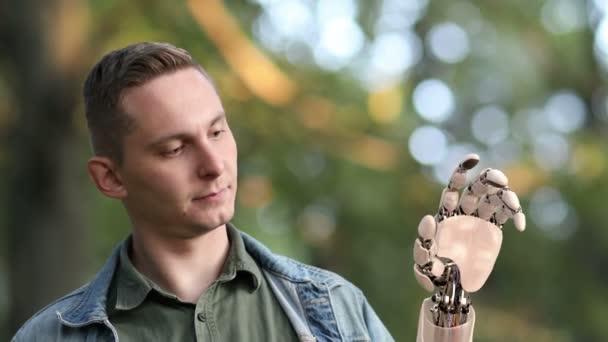 O jovem olha para a sua mão robótica no parque. Bela animação 3D realista. 4K — Vídeo de Stock