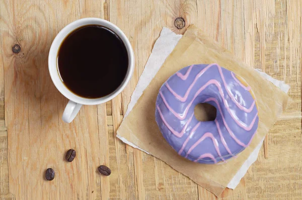 一杯咖啡和一个紫色釉的甜甜圈在老木背景上 顶部视图 — 图库照片