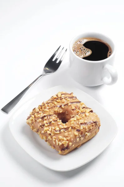 方形甜甜圈与焦糖釉 烤坚果和巧克力条纹在板材和一杯咖啡在白色背景 — 图库照片
