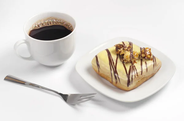 用奶油釉的正方形形状的甜甜圈用烤玉米和巧克力条纹和杯咖啡装饰在白色背景上 — 图库照片