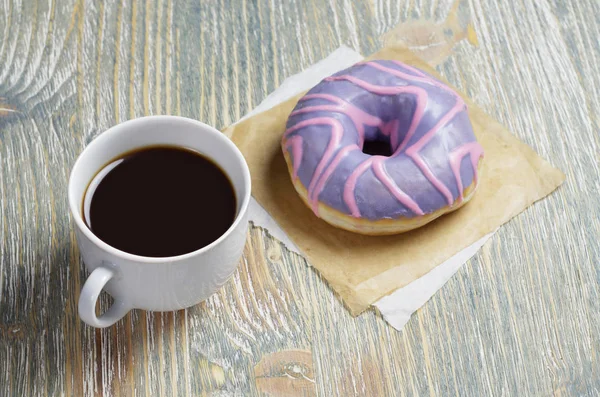 一杯咖啡和一个老木背景上有紫罗兰釉的甜甜圈 — 图库照片